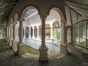 Photographie d'une piscine entourée de piliers, abandonnée.