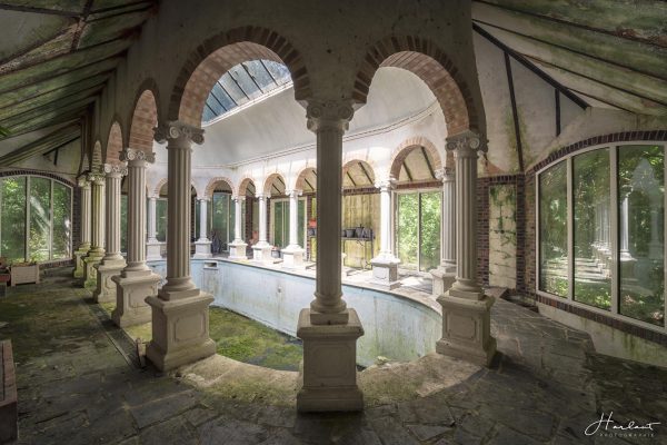 Photographie d'une piscine entourée de piliers, abandonnée.
