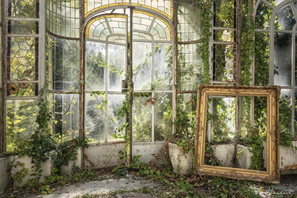 Photographie d'un cadre doré placé dans une pièce vitrée.