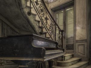 Photographie d'un piano au pieds d'un escalier abandonné.