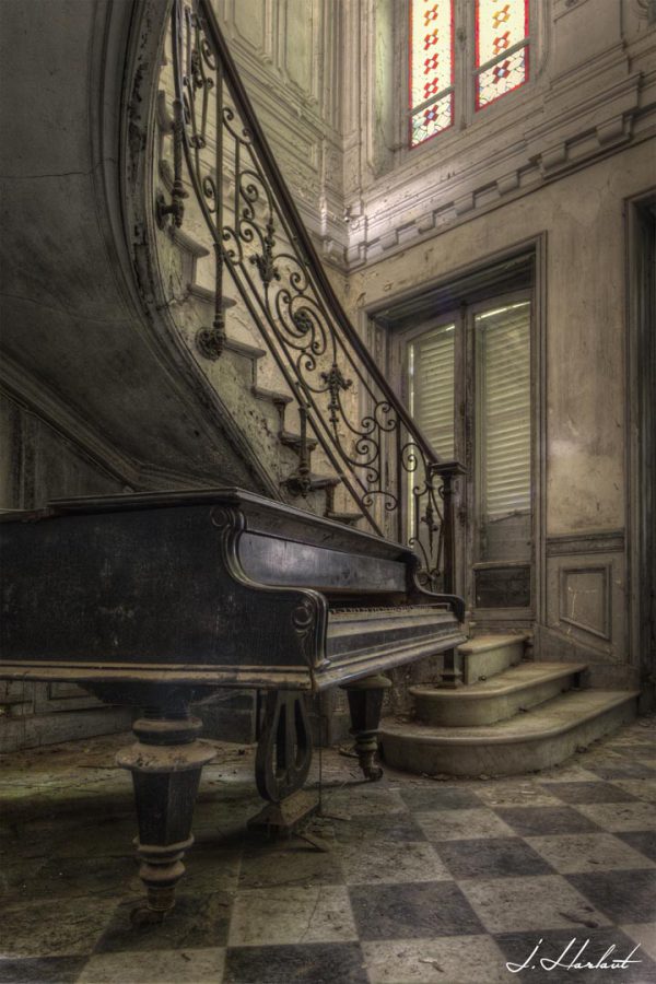 Photographie d'un piano au pieds d'un escalier abandonné.