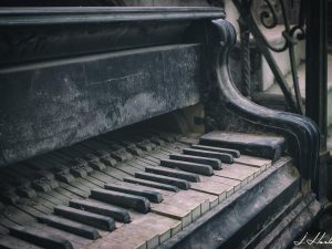 Photographie d'un piano endommagé par le temps au pieds d'un escalier.