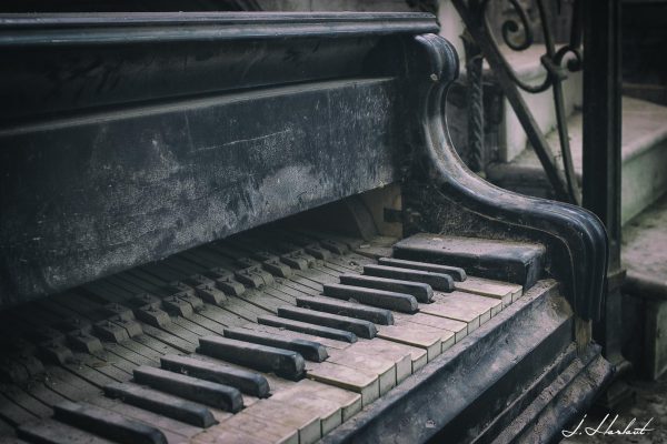 Photographie d'un piano endommagé par le temps au pieds d'un escalier.