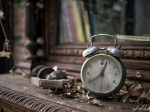 Photographie d'un réveil placé sur un meuble dans un espace abandonné. Exempt de mouvements, figé dans le temps.