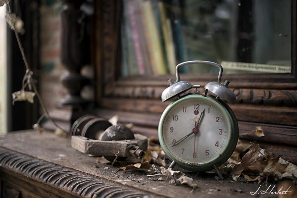 Photographie d'un réveil placé sur un meuble dans un espace abandonné. Exempt de mouvements, figé dans le temps.