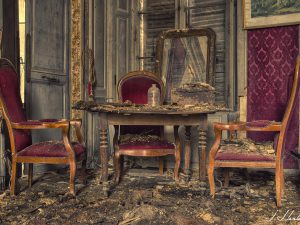 Photographie d'une table et de chaises abîmées par le temps dans une maison partiellement détruite.
