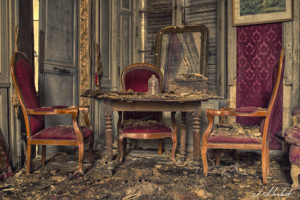 Photographie d'une table et de chaises abîmées par le temps dans une maison partiellement détruite.