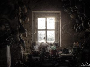 Photographie de vieux vases et vaisselles placées sur un meuble devant une fenêtre.