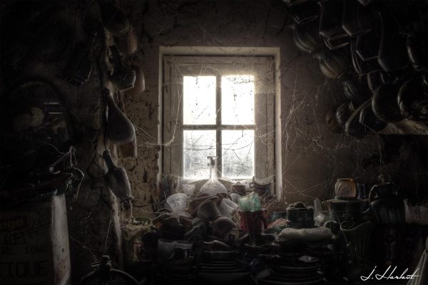 Photographie de vieux vases et vaisselles placées sur un meuble devant une fenêtre.